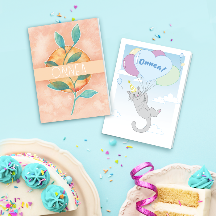 Kaksi onnittelukorttia ja syntymäpäiväkakku vaaleansinisellä taustalla.