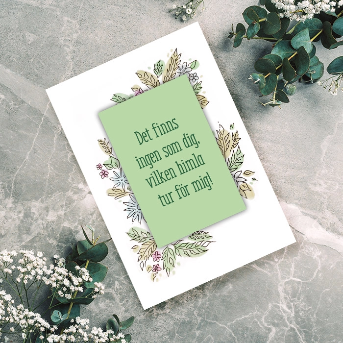 Ett kort med blommor och blad med en text som visar omtanke, liggandes på en grå bakgrund