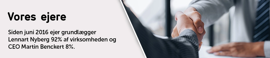 To personer i jakkesæt giver hinanden hånd over et skrivebord, som symbol på en forretningsaftale eller et samarbejde.