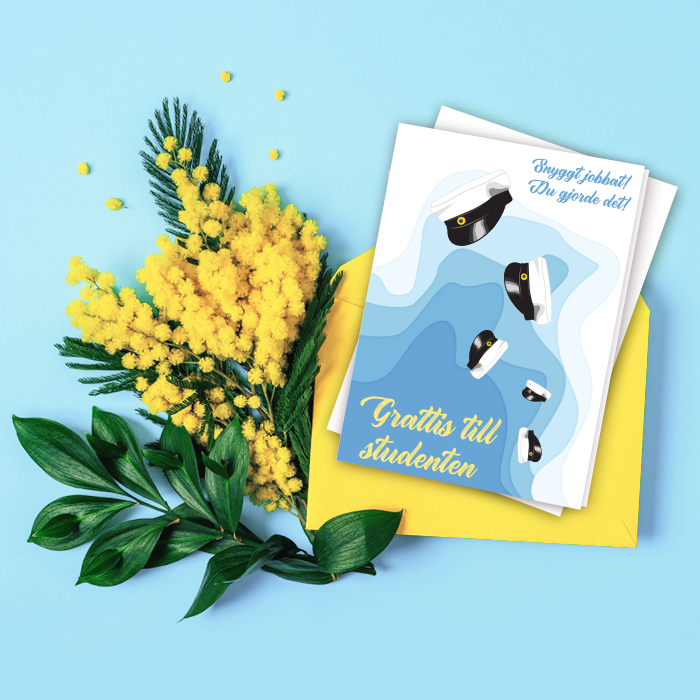 Ett blått och vitt kort med flygande studentmössor, liggandes på en blå bakgrund med gula blommor