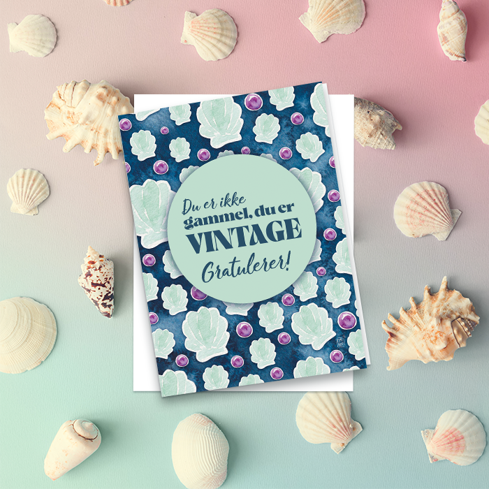 Gratulasjonskort med havdesign, liggende på en pastellfarget bakgrunn med skjell.